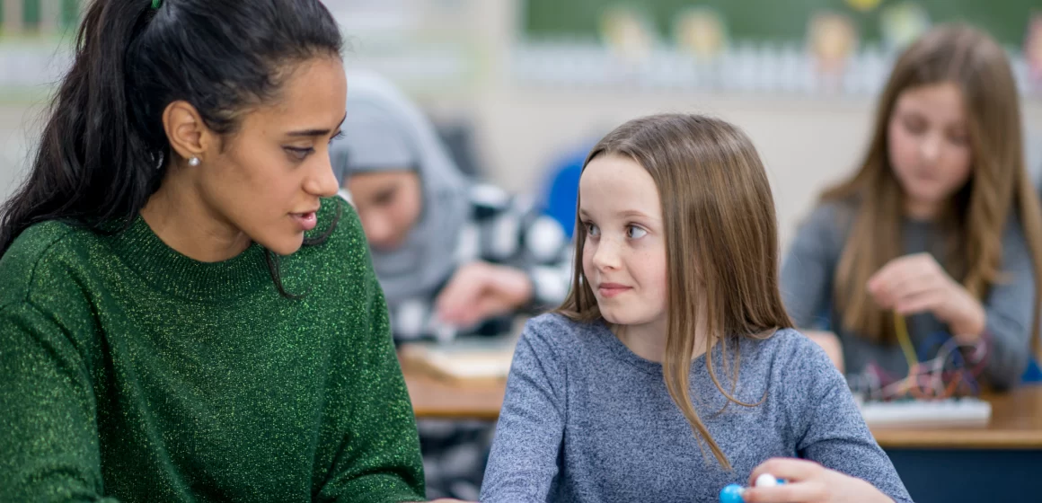 A teacher helping a young girl in a classroom.
