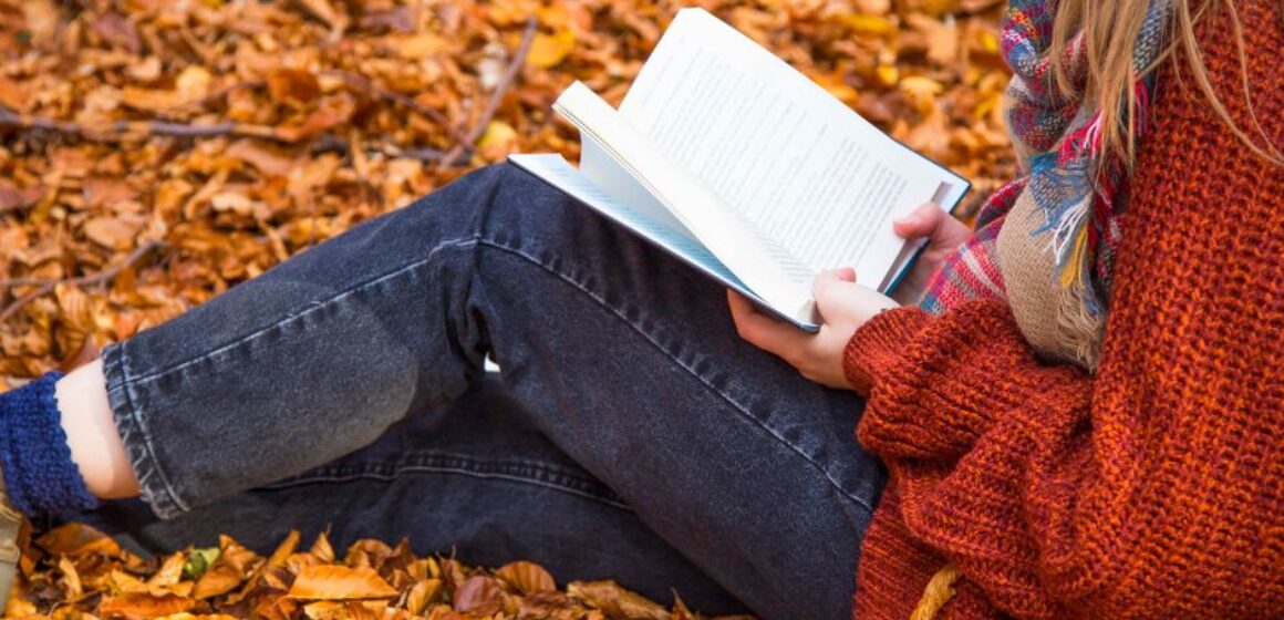 A woman reading a book in the autumn leaves.