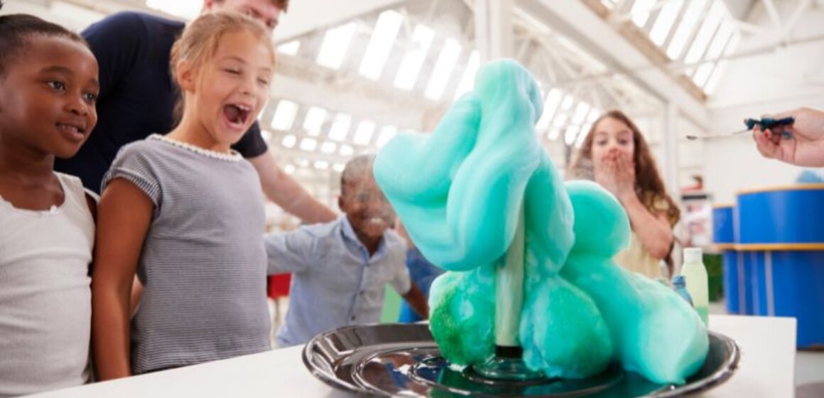 A group of children are conducting a STEM activity as they observe a blue liquid on a plate.